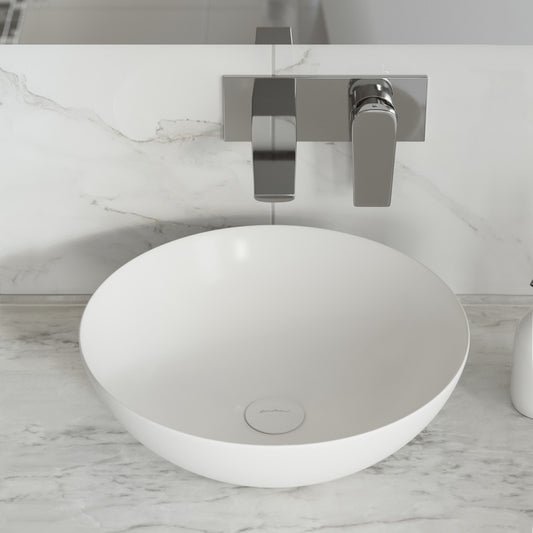 Shiny white ceramic vessel sink with round shape on marble countertop and wall-mounted chrome faucet.