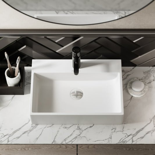 Rectangular white ceramic vessel sink with center drain on marble countertop, black faucet above.